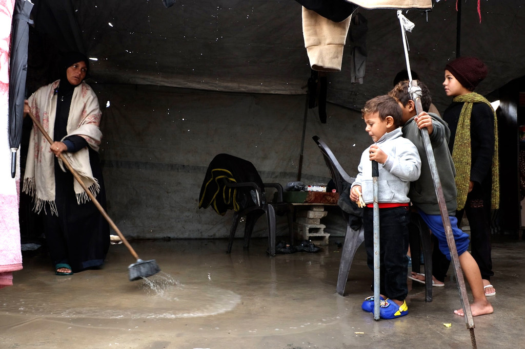 نازحة تقوم بدفع مياه الأمطار خارج خيمتها التي غمرتها سيول الليلة الماضية، بينما يقف أطفالها إلى جانبها في أحد مواقع النزوح في غزة، في وقت تفاقمت فيه الظروف المعيشية القاسية أصلا.